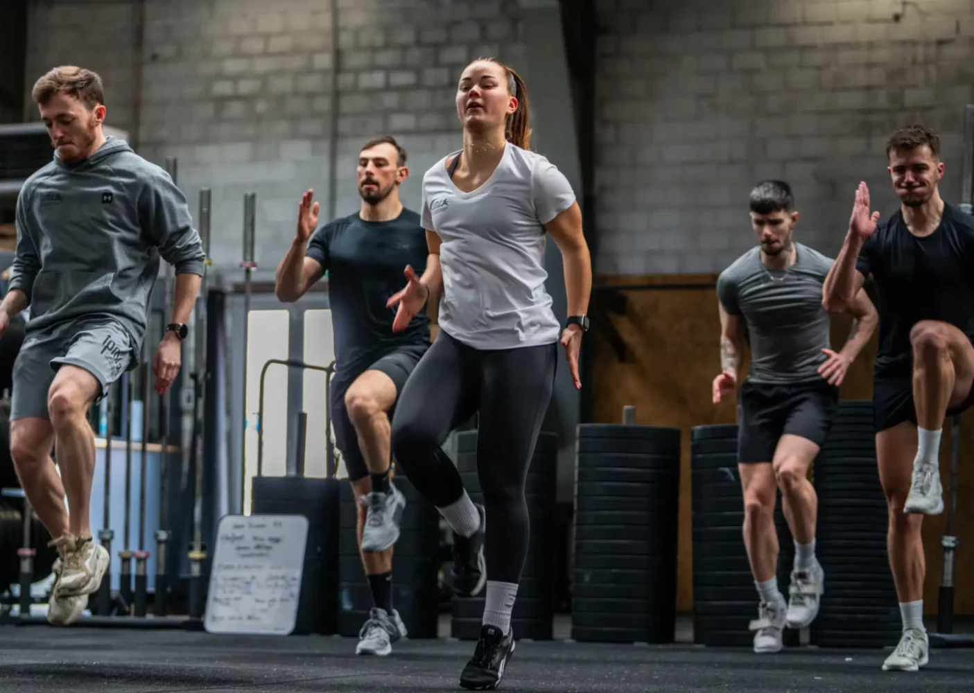 Groupe de stagiaires réalisant un exercice de montées de genoux dynamiques lors d'un cours collectif en salle de cross-training