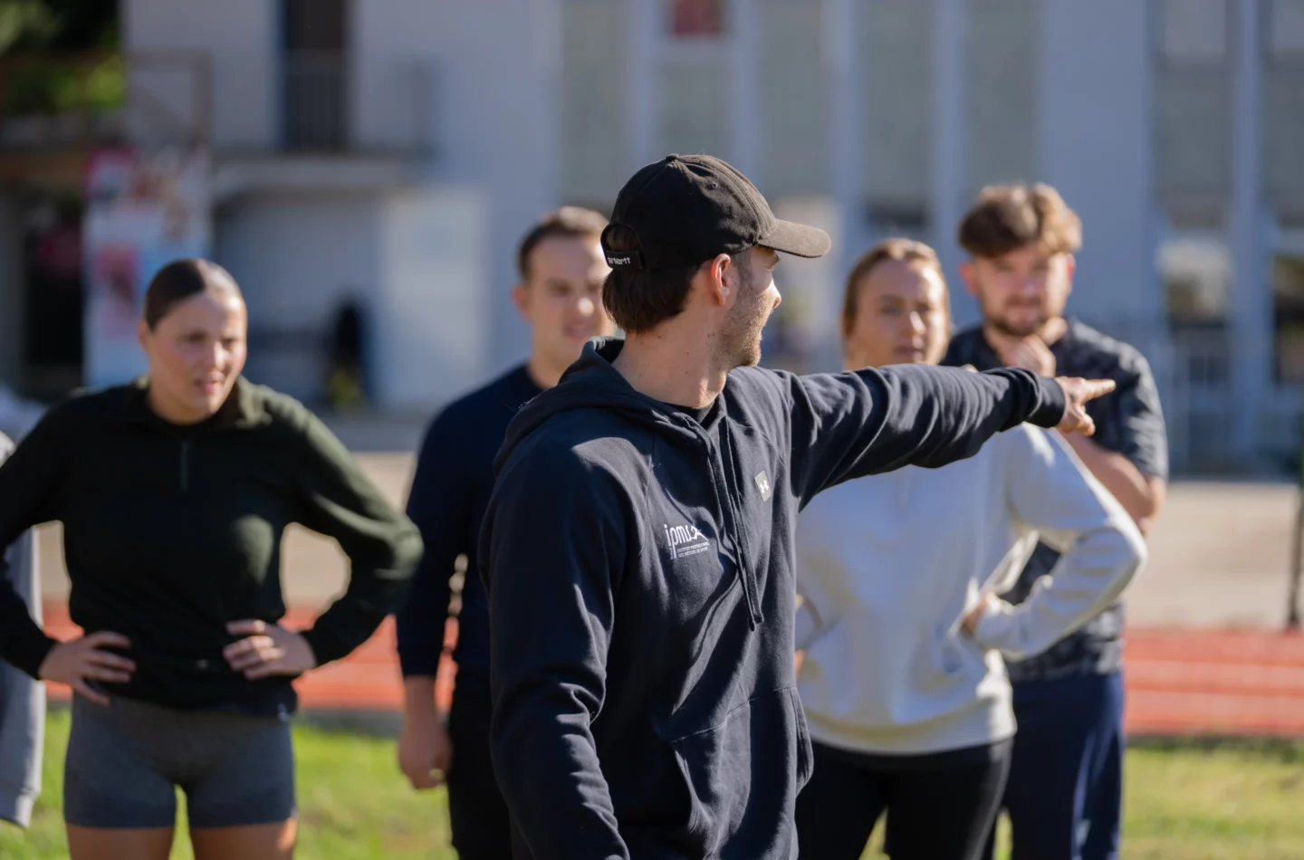 Formateur IPMS en sweat à capuche donnant des consignes à un groupe de stagiaires sur un terrain extérieur