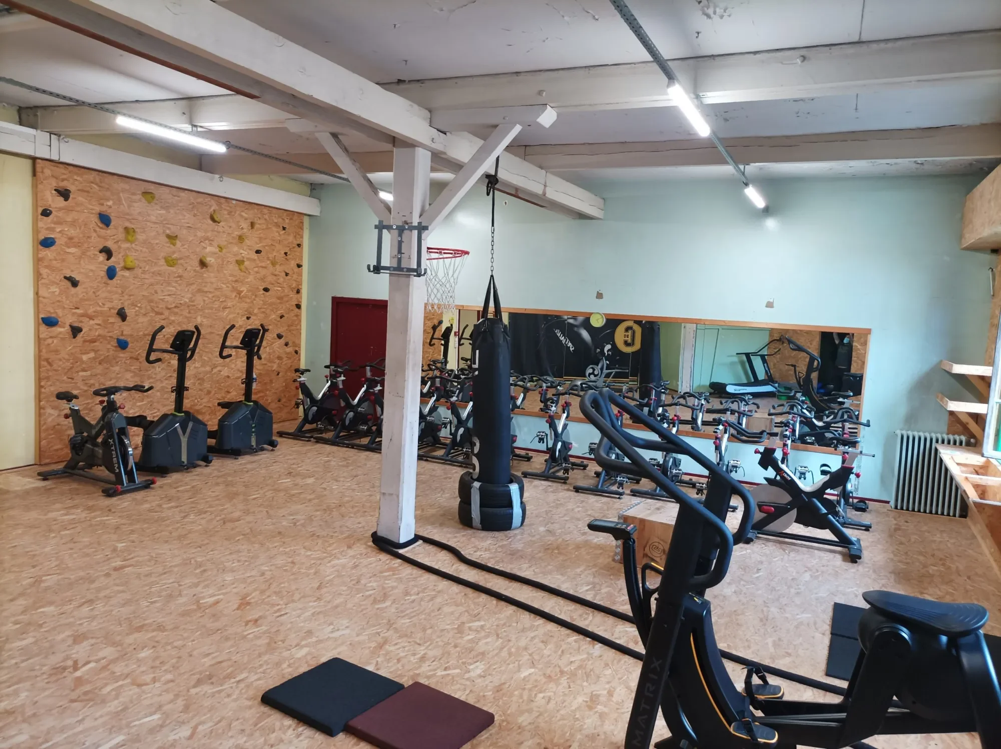 Salle d’entraînement IPMS Limoges avec mur d’escalade, vélos et sac de frappe.