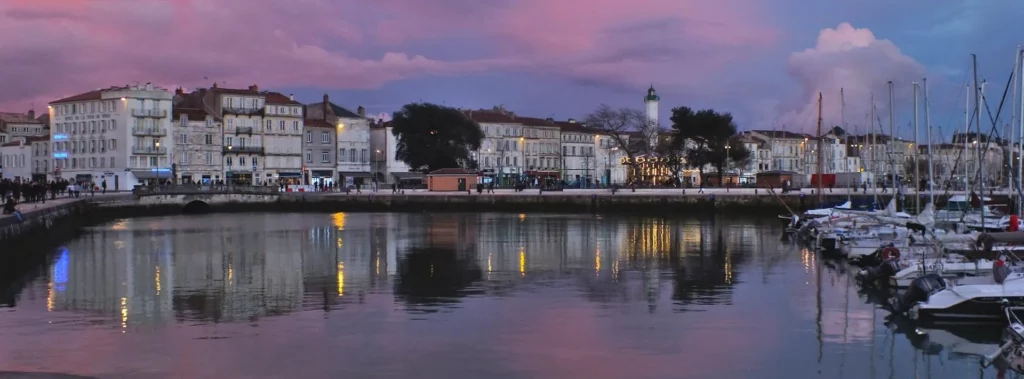Vue du Vieux-Port de La Rochelle au coucher du soleil, avec les tours et les voiliers amarrés.