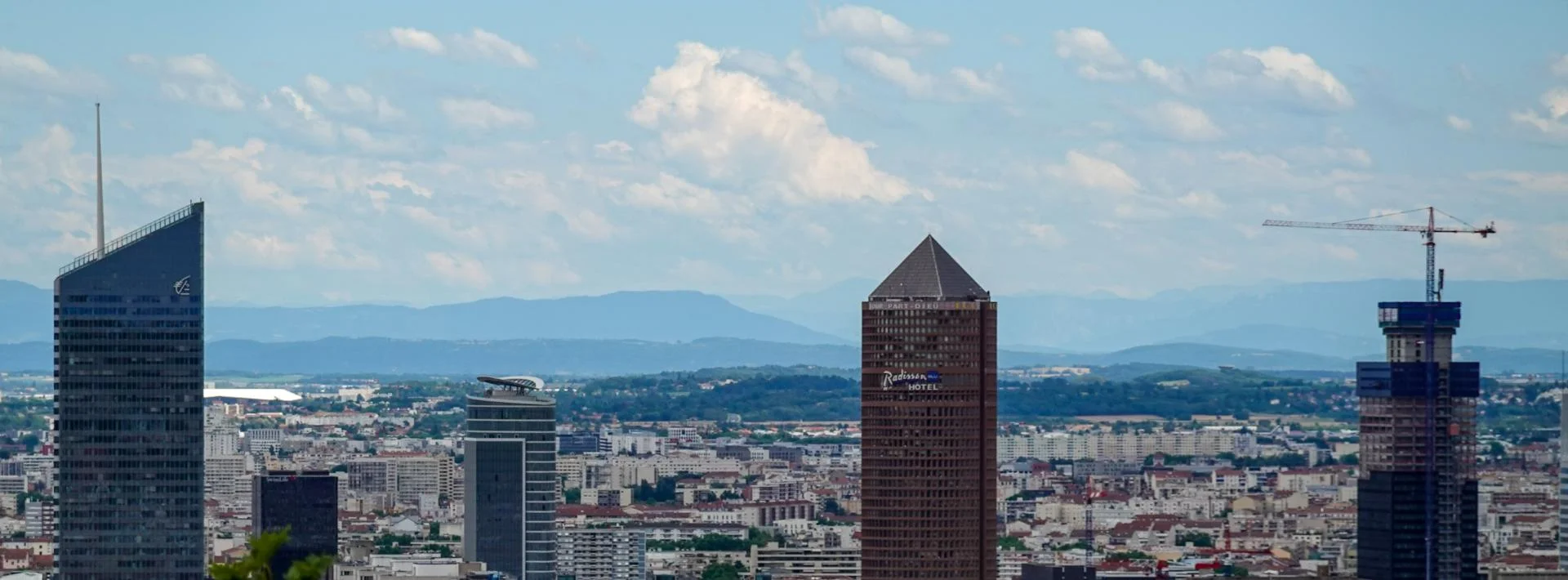 Vue panoramique du quartier de la Part-Dieu à Lyon avec ses tours emblématiques et les Alpes en arrière-plan.