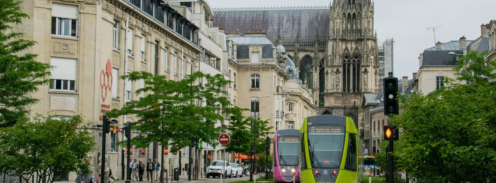 Vue urbaine de Reims, tramway vert et cathédrale en arrière-plan.