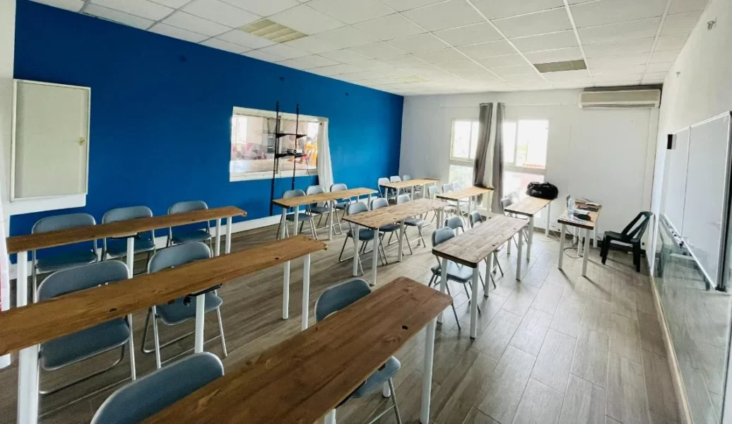 Salle de cours IPMS Saint-Louis avec tables en bois clair et mur bleu pédagogique.