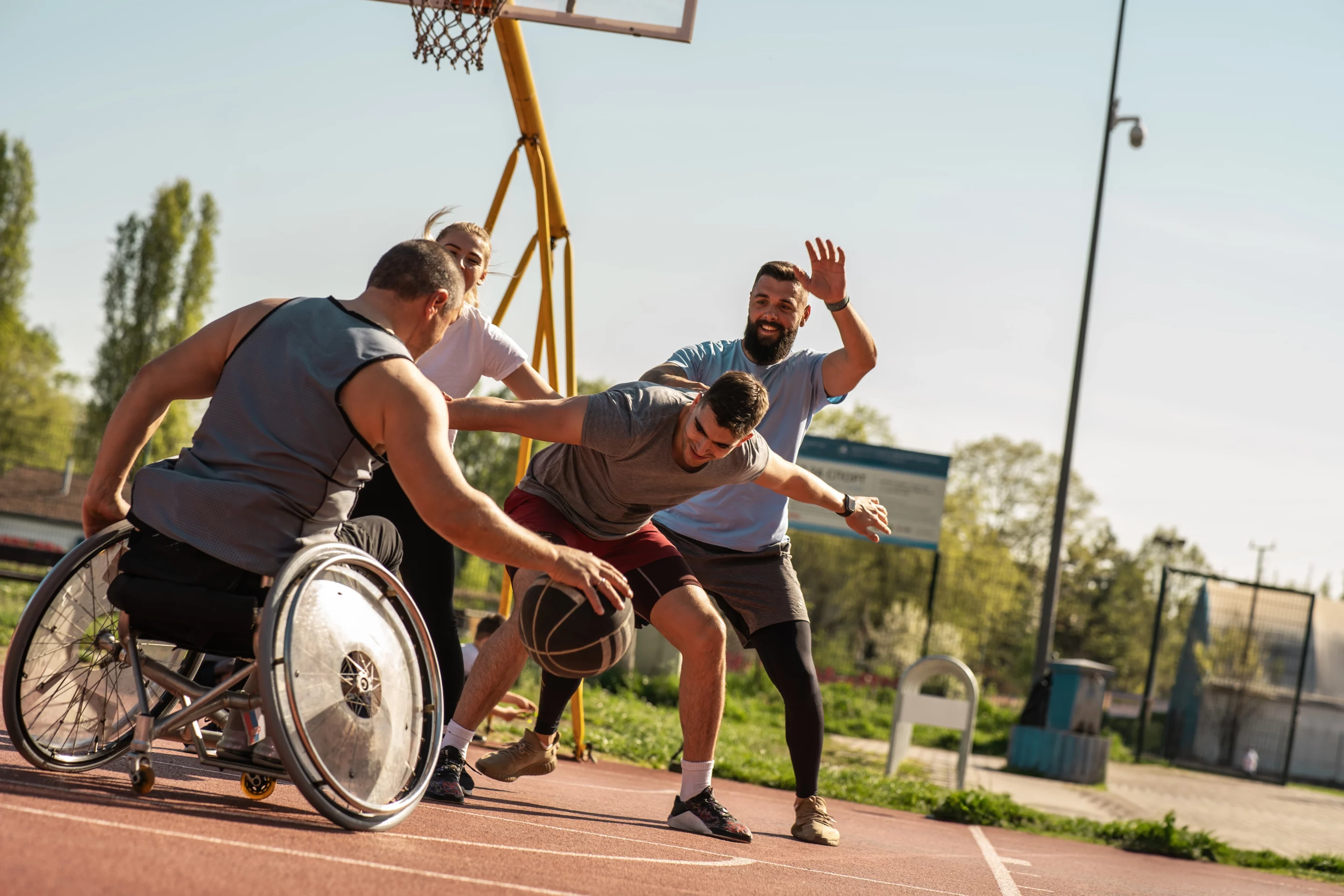 Séance de basket inclusif réunissant des joueurs valides et un joueur en fauteuil sur terrain extérieur.