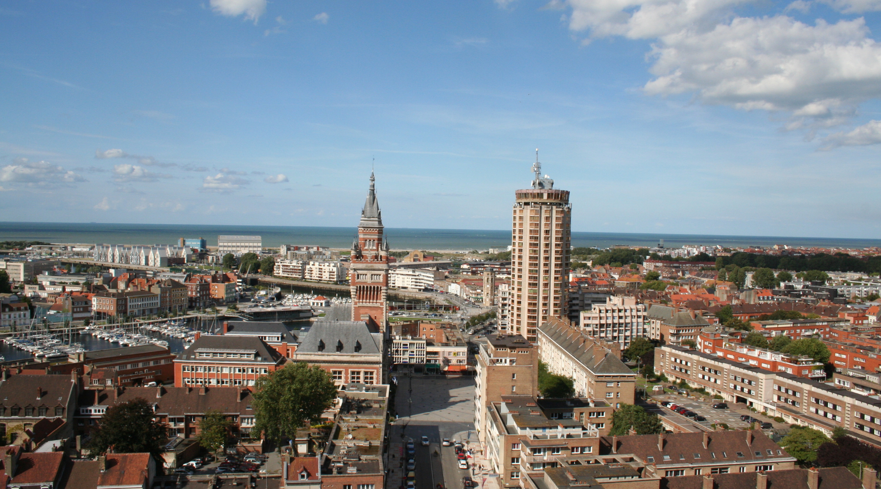 Vue aérienne de Dunkerque montrant le beffroi, la tour du Leughenaer, le port et la mer en arrière-plan sous un ciel clair.