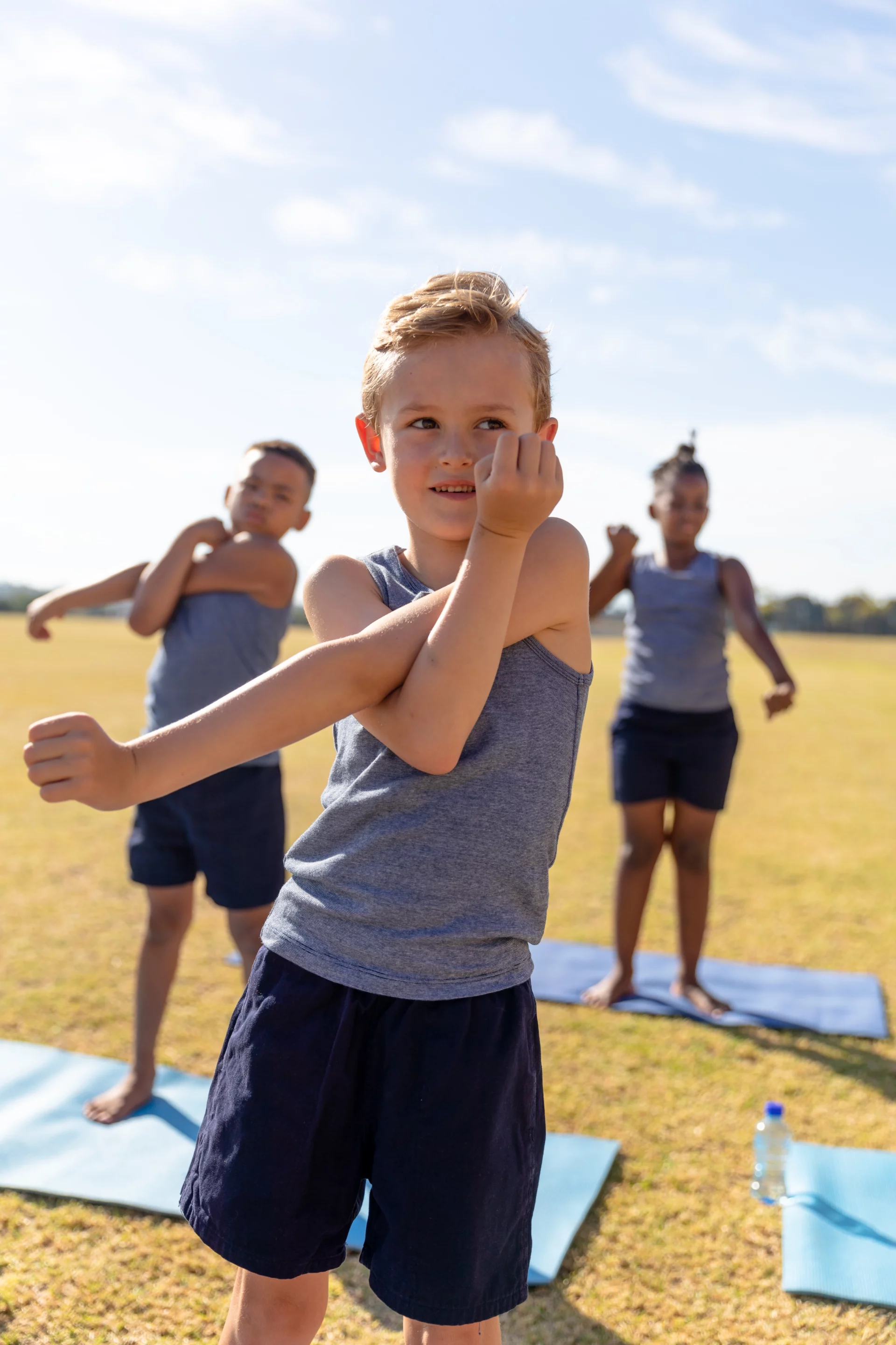 Enfants réalisant des étirements sur tapis lors d’une initiation sportive en plein air.