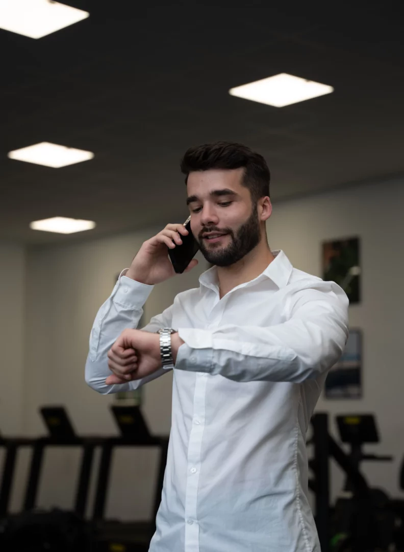 Technico-commercial en situation professionnelle passant un appel tout en consultant son horaire dans un environnement sportif.