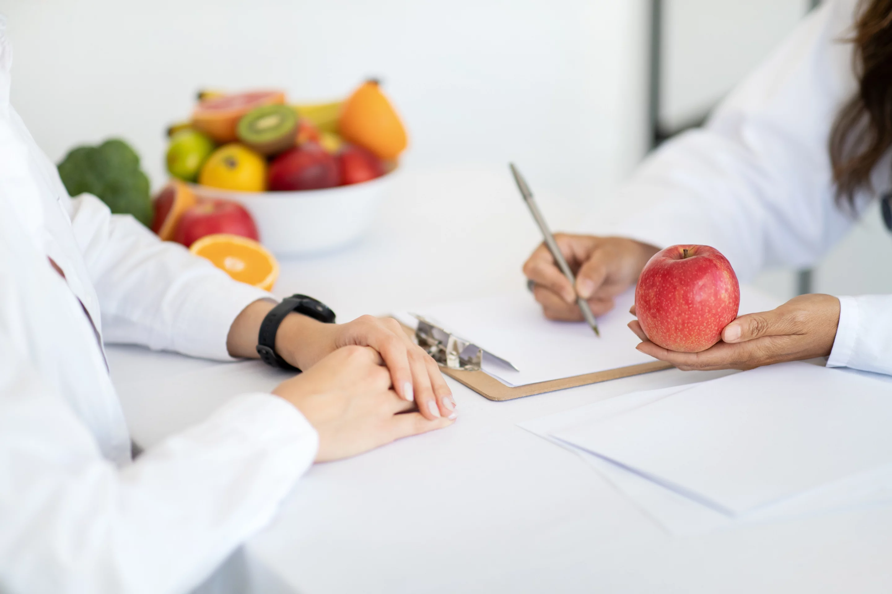 Consultation diététique : diététicienne prenant des notes en tenant une pomme, illustrant la réalisation d’un bilan nutritionnel.