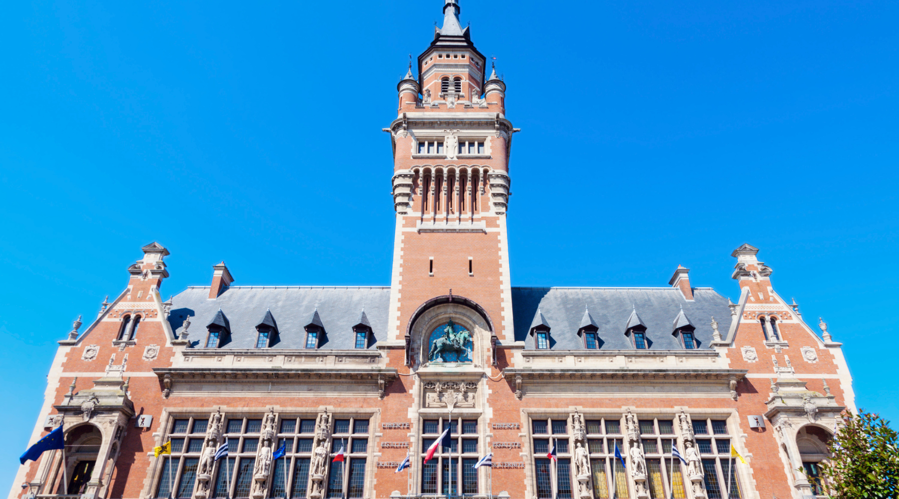 Façade du beffroi de Dunkerque en briques rouges, vue frontale sous un ciel bleu dégagé.