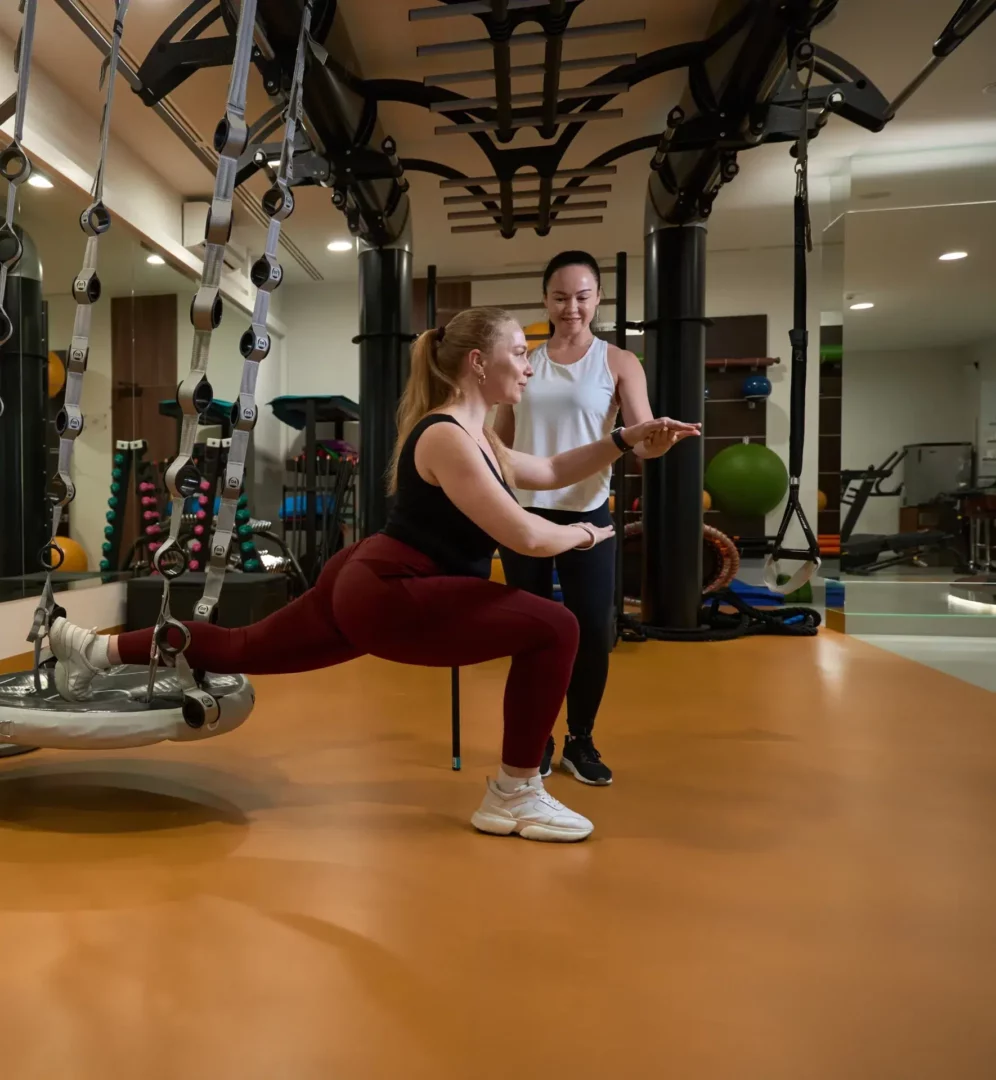 Coach sportif BPJEPS APSF encadrant une séance de coaching individuel en centre de remise en forme - exercice de fente sur équipement fonctionnel