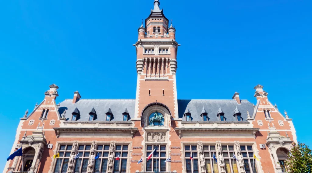 Façade du beffroi de Dunkerque en briques rouges, vue frontale sous un ciel bleu dégagé.